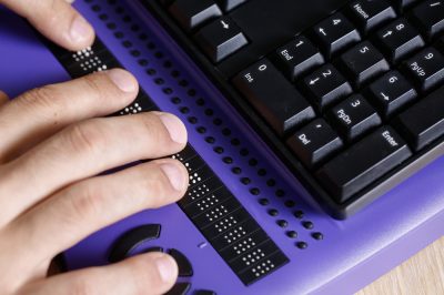 hands on a refreshable braille keyboard attached to a computer
