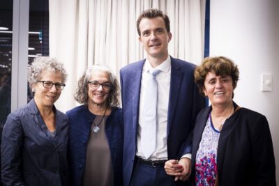 3 white woman and one white man smiling into camera.  The man is more than one foot taller than the women