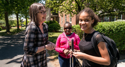 Two Black blind women students with long canes and one white woman on a college campus