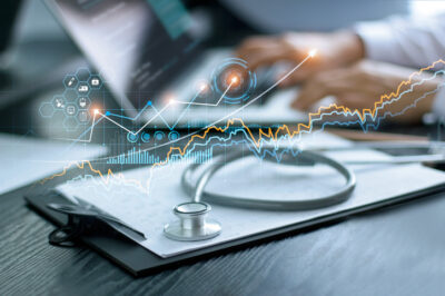 a stylized image to represent the intersection of health care and technology, with a stethoscope resting on a clipboard and a computer in the background with electronic imaging waves across the picture