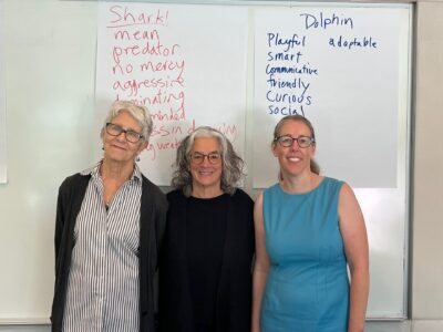 Lainey Feingold with Melinda Bird and Autumn Elliot of Disability Rights California standing in front of two large sheets of paper listing words related to sharks and dolphins 