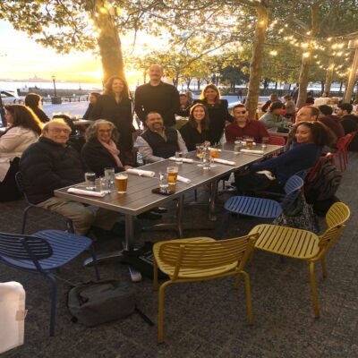 a dozen people around an outdoor table smiling at the camera