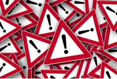 a pile of triangular warning signs. The white triangle has a red border with a large black exclamation point in the center