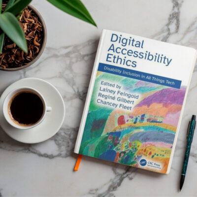 An aerial view of the Digital Accessibility Ethics Book on a clean desk with a green plant and a cup of coffee and pen.