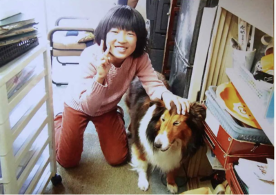 A smiling, 11-year-old Japanese girl resting her hand on a neighbor's pet dog.