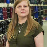 Chancey Fleet, a white woman who is blind standing in front of shelves of library books