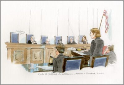 A courtroom sketch of Karla Gilbride, a white woman, standing at the lectern giving an argument to the U.S. Supreme Court justices. The sketch shows her hands on her Braille notes with an arrow indicating “Braille.” The sketch also shows Karla’s co-counsel taking handwritten notes, her opposing counsel listening, and Justice Thomas’s empty chair among those of the other seated justices, indicating that he was not present for the argument. There are American flags in the background.